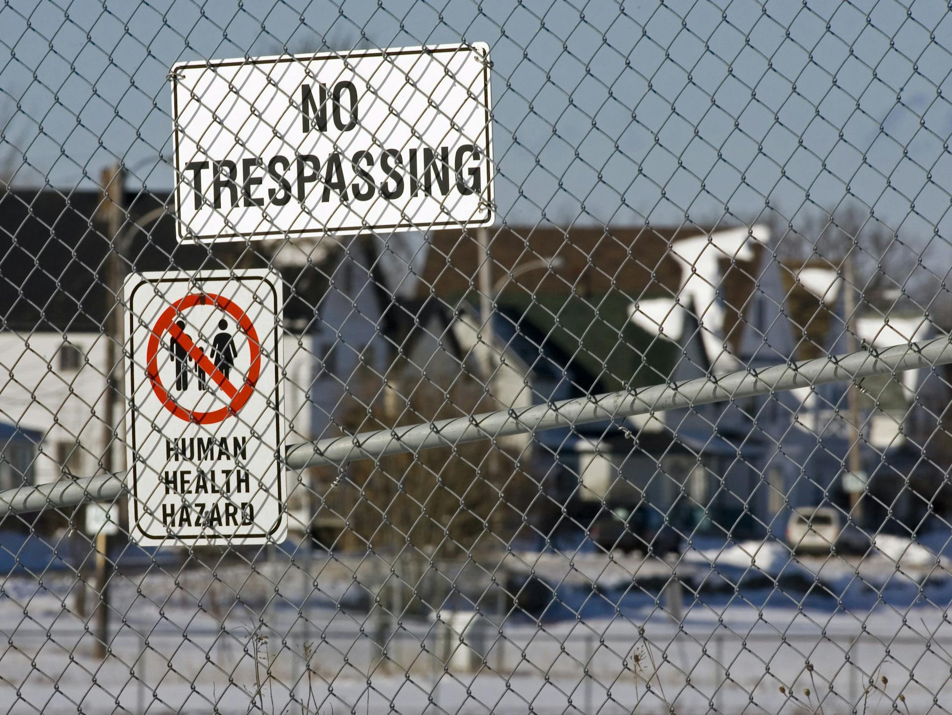 Chain-link fence with 'no trespassing' and 'human health hazard' signs