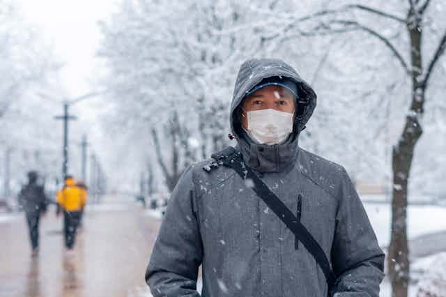 Un hombre abrigado y con mascarilla pasea por un parque nevado.