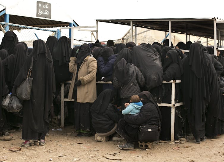 Women in black niqabs and hijabs waiting together in a crowd