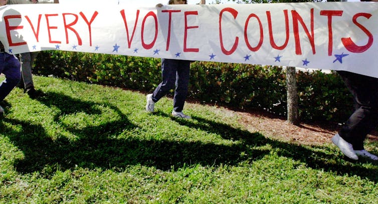 A white sign with red text that says 'Every Vote Counts.'
