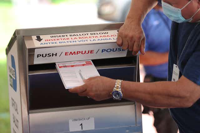 A man inserting a ballot into a silver ballot box. 