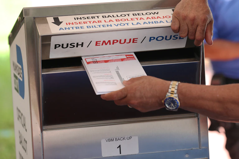 A man inserting a ballot into a silver ballot box.