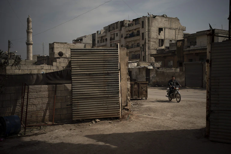 A man rides a motorbike near the rubble of buildings in Syria.