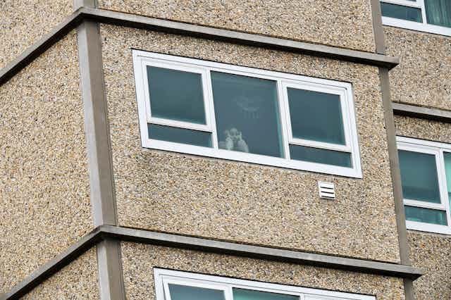 A child looks out of the window of a high-rise apartment under lockdown