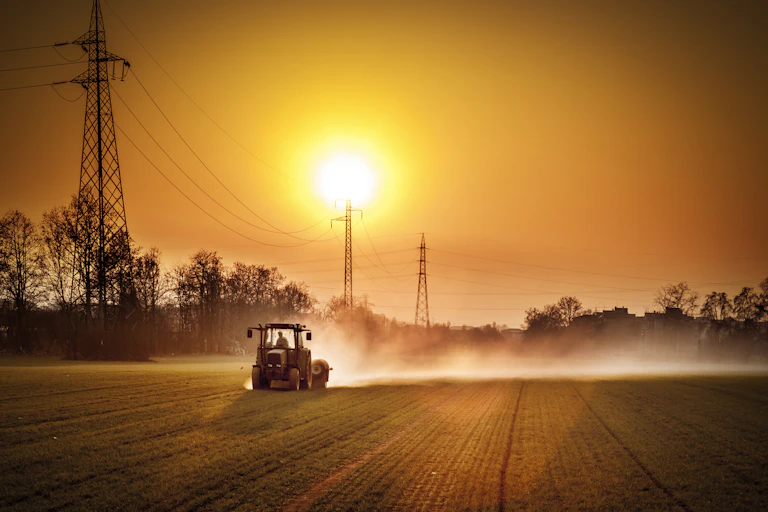 A tractor on a dusty field at sunset.