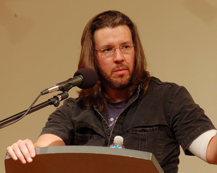 Bearded man giving lecture with microphone and lectern.