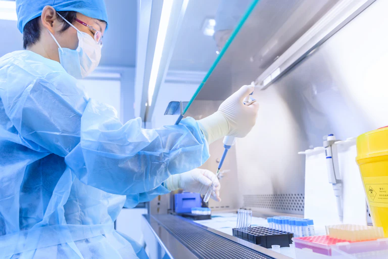A womane wearing protective equipment handles a test tube in a lab.