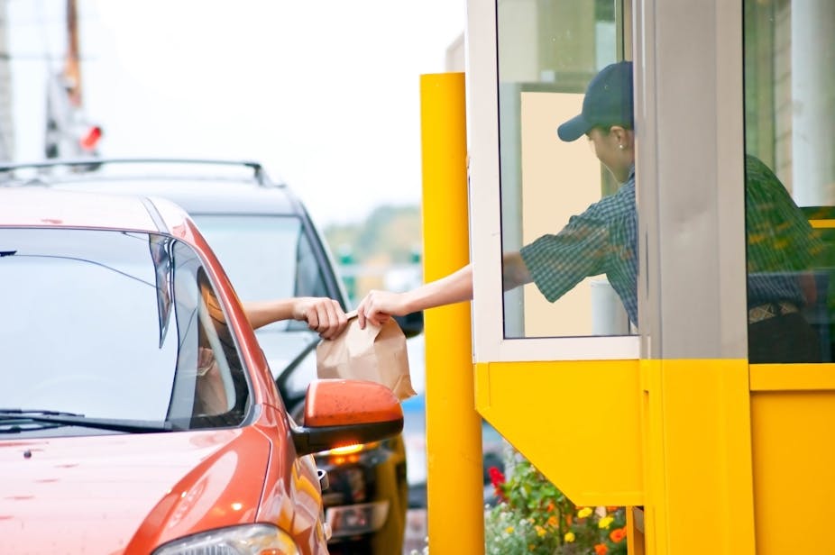 A worker at a fast food drive-through window hands a paper bag filled with food to a customer in their car.