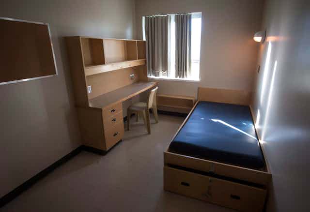 An empty cell with a cot, desk and bulletin board