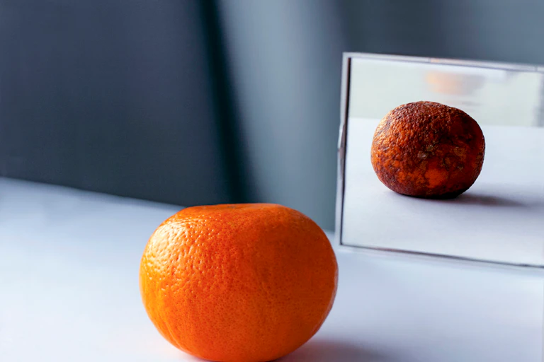 A fresh orange is placed in front of a mirror, while its reflection is aged