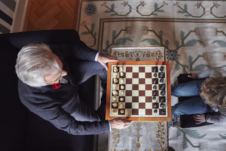 An elderly man plays chess with a child.