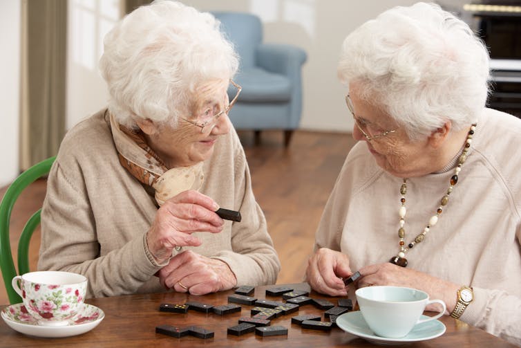 Two elderly women playing with dominoes.