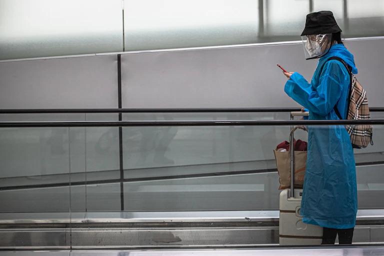 A woman on an airport travelator wearing a face mask and a visor.