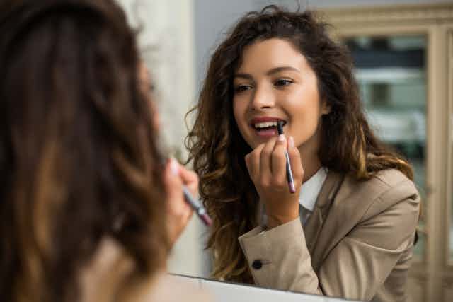 Office woman applying lipstick at mirror