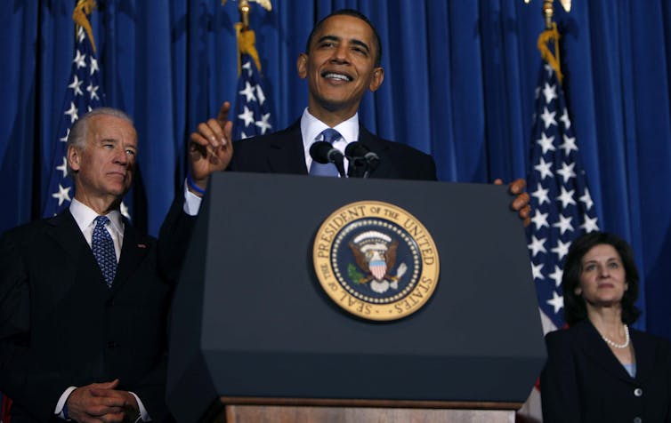 Barack Obama in front of a lectern with Joe Biden behind.