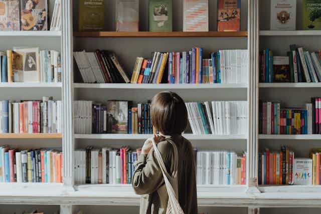 Woman in bookshop standing near white wooden book shelf