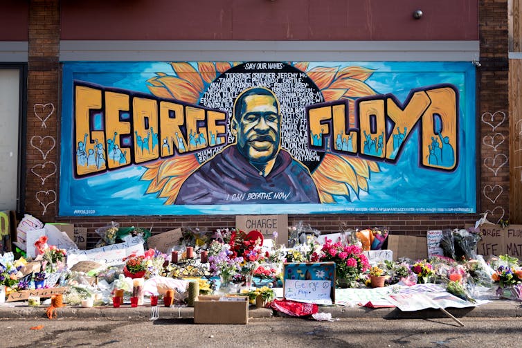 Mural on wall of George Floyd with flowers and cards in front.