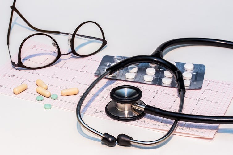 An ECG printout, stethoscope, eyeglasses and medication.
