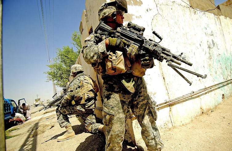 US army soldier stands guard at damanged street corner.