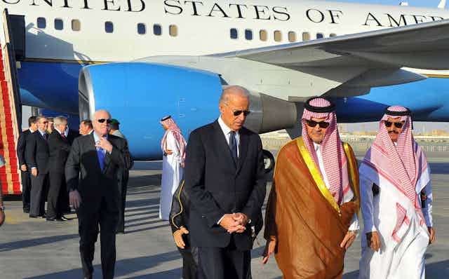 Biden walks with two Saudi men at an airport, with Air Force Two visible in the background