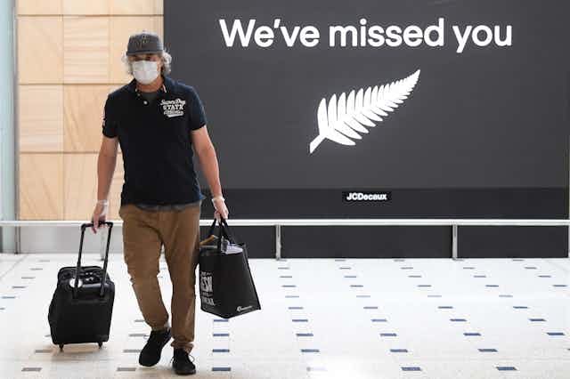 A man, at Sydney airport, walks passed a sign saying "We've missed you" with the New Zealand silver fern
