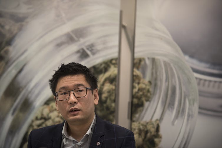 A man talks with a photo of cannabis behind him.