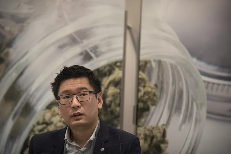 A man talks with a photo of cannabis behind him.