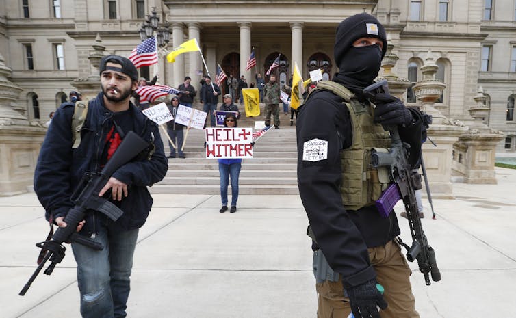 In this April 2020 photo, protesters carry rifles near the steps of the Michigan State Capitol building in Lansing, Mich. A plot to kidnap Michigan’s governor has put a focus on the security of governors in the United States. (AP Photo/Paul Sancya)