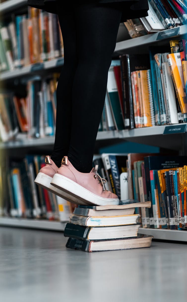 Girl uses stands on a stack of books