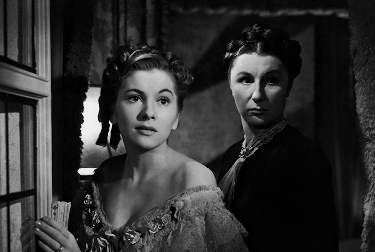 Older woman and younger woman look in mirror, scene for black and white film.