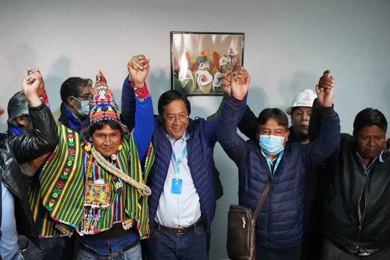 Men including Luis Arce raise their hands in celebration.