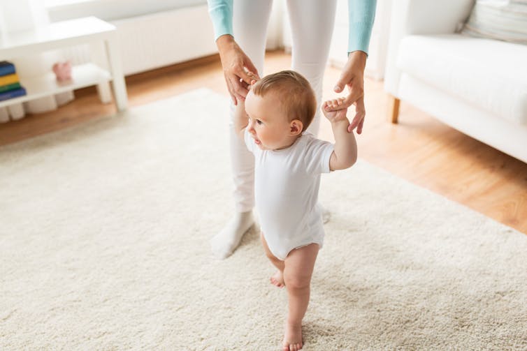 Mother holds baby's hands to help them walk.