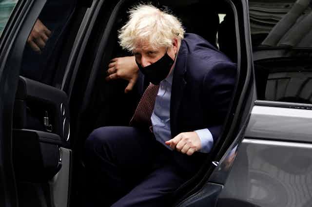 Boris Johnson gets out of a car, wearing a mask