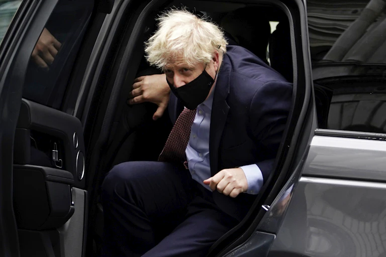 Boris Johnson gets out of a car, wearing a mask