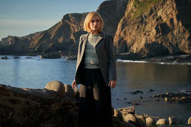 Rebecca stands on a Cornish beach with cliffs behind her.