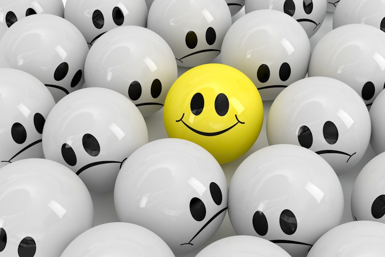 A yellow ball with a smiley face among several grey balls with frowny faces