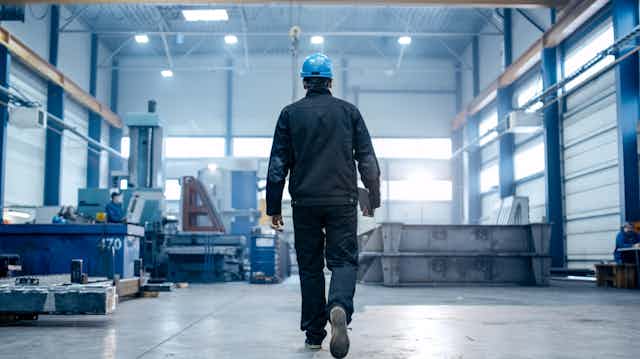 Un trabajador de espaldas dirigiéndose a su puesto en una fábrica.