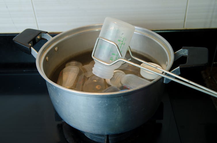 A pair of tongs lifting a plastic baby bottle from a boiling pan.