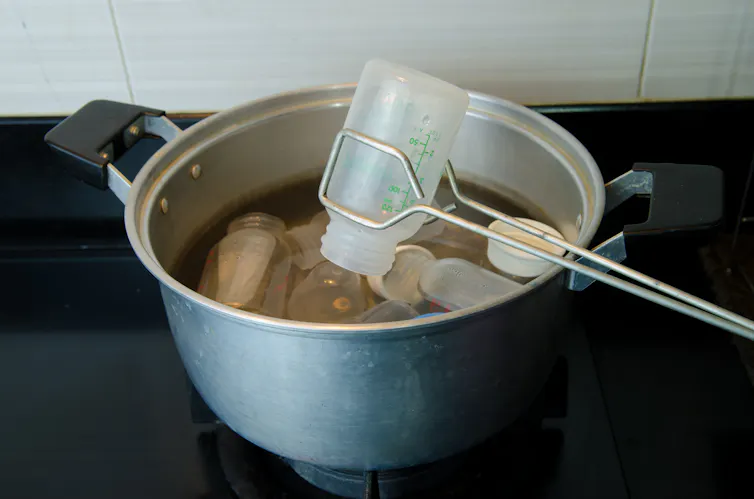 A pair of tongs lifting a plastic baby bottle from a boiling pan.