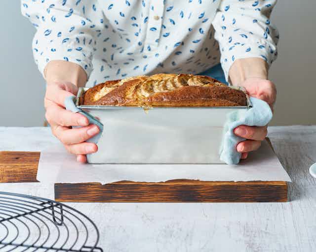 Baking tin of banana bread in woman's arms.