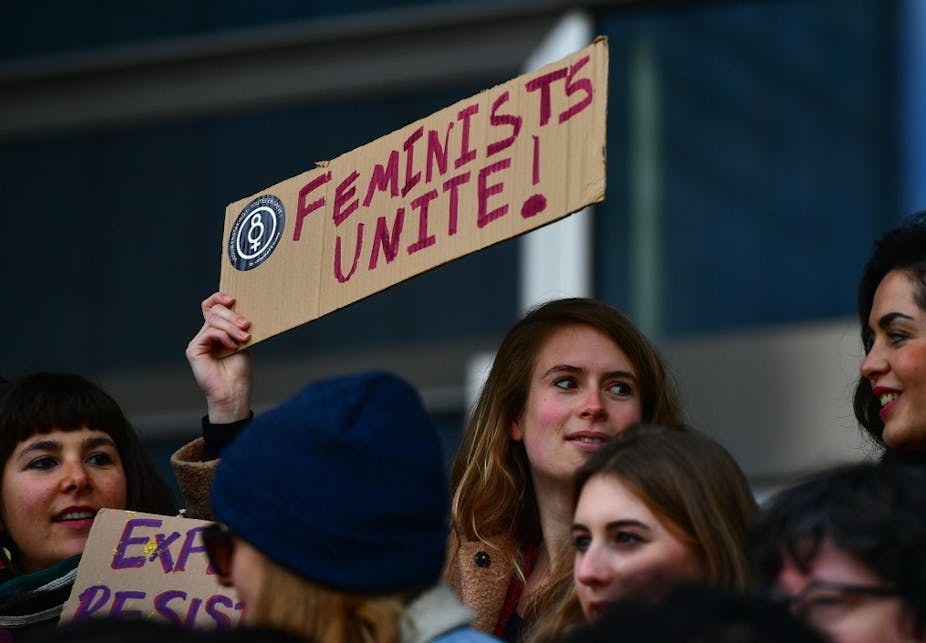 Une femme tient une affiche sur laquelle on peut lire "Les féministes s'unissent !"