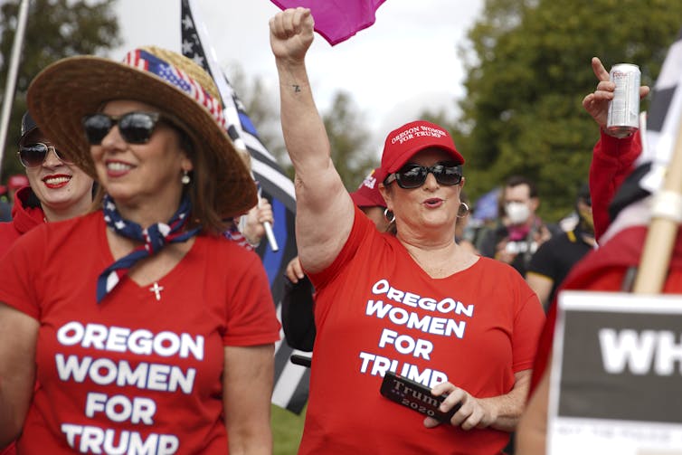 Two women are cheering as they wear red T-shirts with the words Oregon Women For Trump