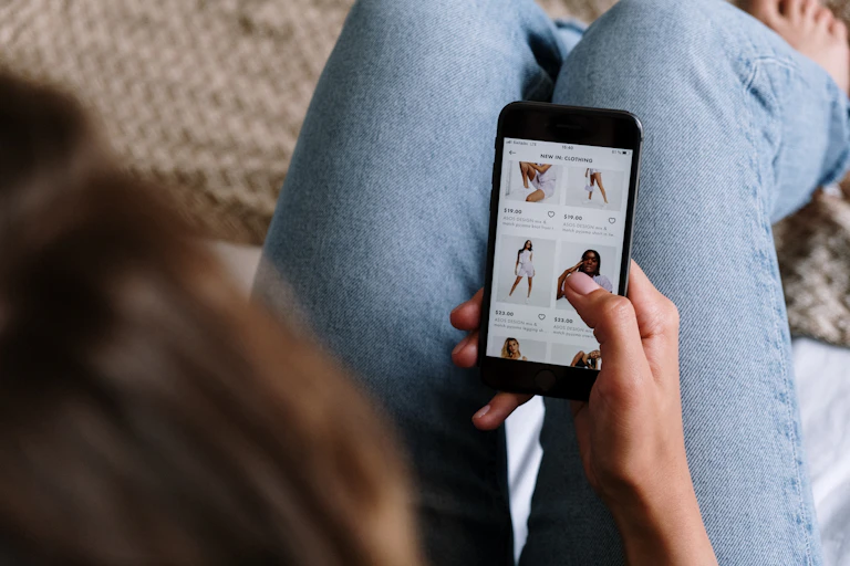 A woman wearing jeans shops on her phone.