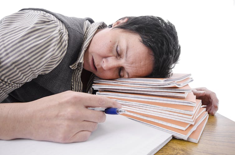 Exhausted female academic rests head on pile of assignments