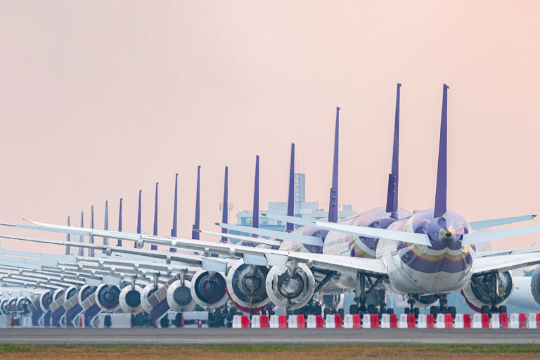 A row of grounded aeroplanes on an airport runway.