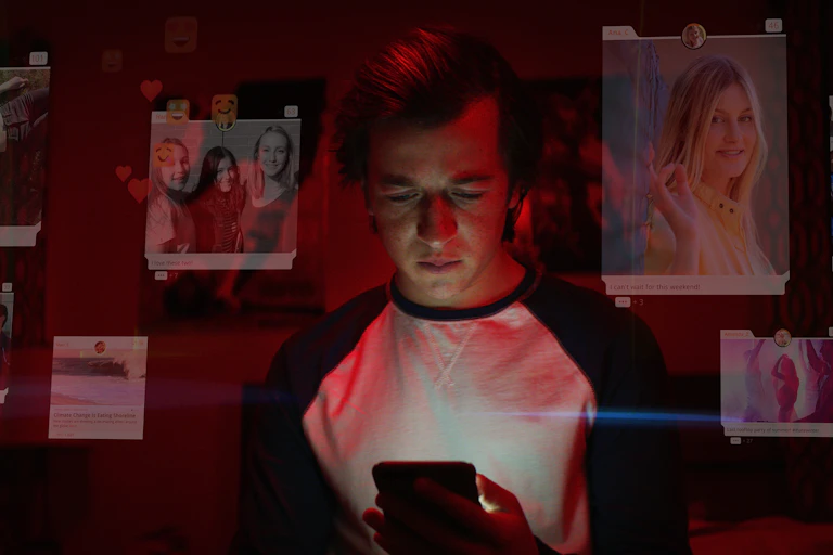 A young man looks at his mobile phone, the screen lighting his face. Around him are graphics showing photos from social media of beautiful young women and messages of fun and friendship.