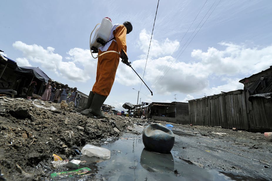 A man in a hazmat suit spraying insecticide in a slum