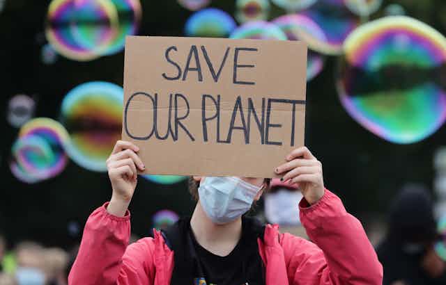 A young protester wearing a mask holds a sign saying 'save our planet'.