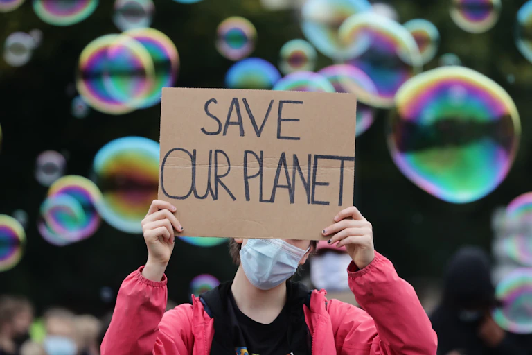 A young protester wearing a mask holds a sign saying 'save our planet'.