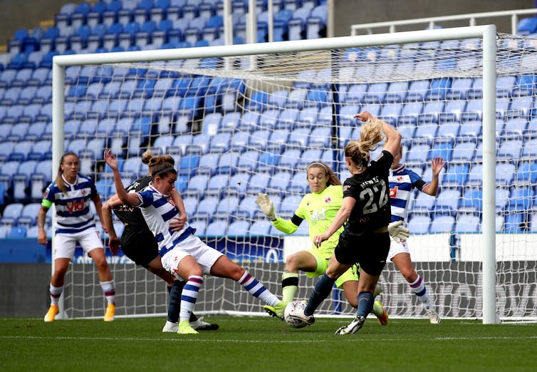 A woman football player shoots at goal surrounded by other players.